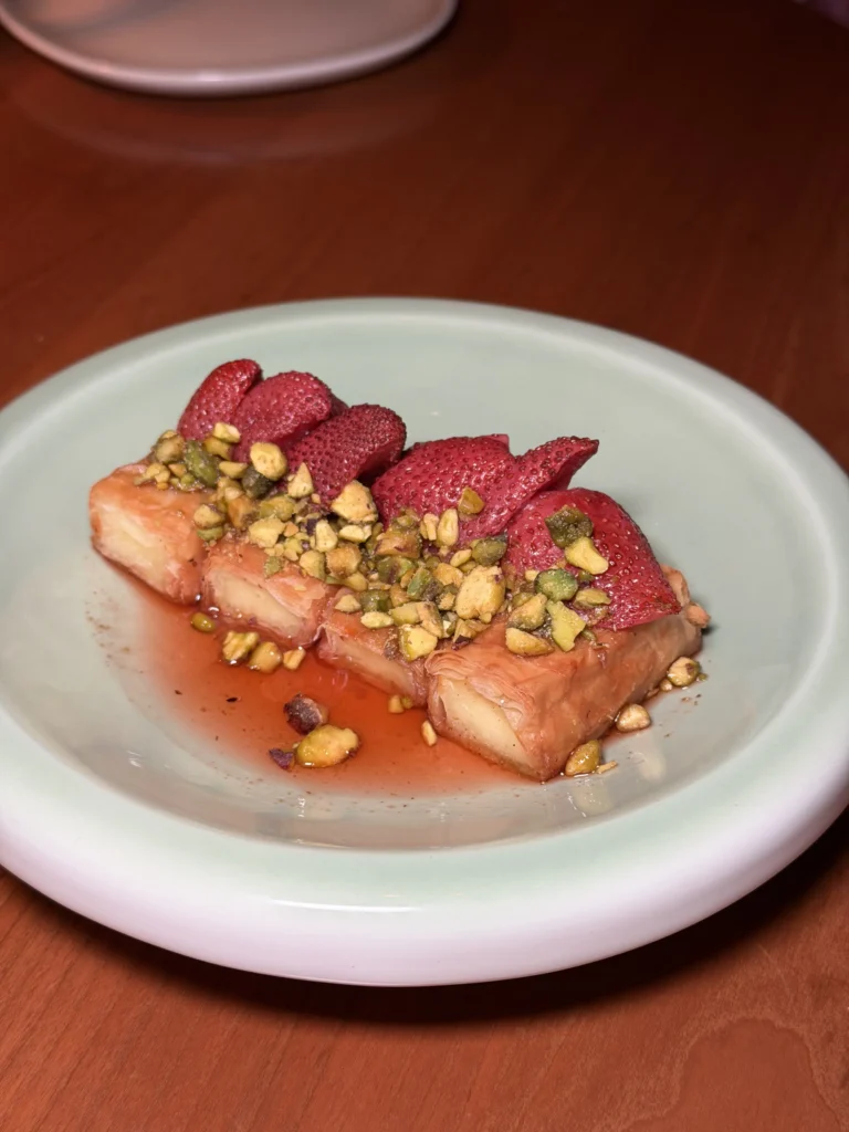 Strawberry baklava halloumi rolls topped with pistachios and sliced strawberries on green plate