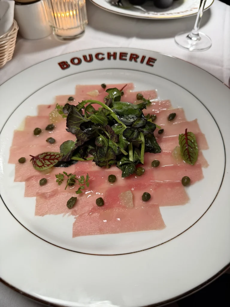 Yellowfin tuna carpaccio with capers and micro greens on branded plate