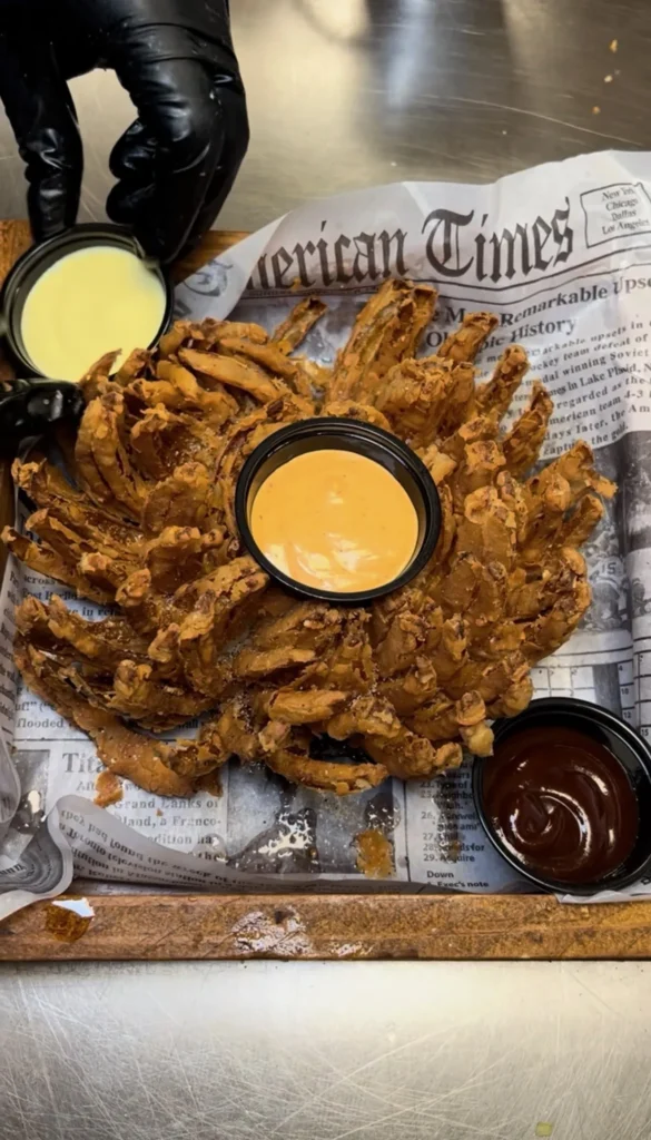 Golden fried blooming onion served with three colorful dipping sauces on newspaper liner