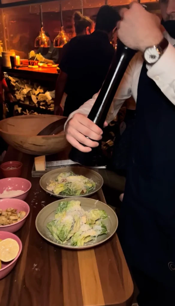 Fresh Caesar salad being prepared tableside with grated parmesan cheese and wooden serving bowls
