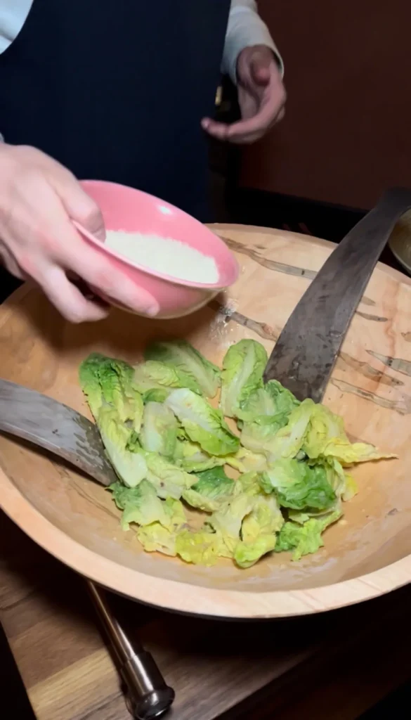 Fresh romaine lettuce being chopped with a knife on wooden cutting board for Caesar salad preparation