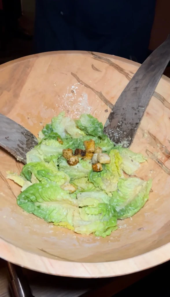 Classic Caesar salad with romaine lettuce, croutons, and parmesan in a wooden bowl with serving utensils