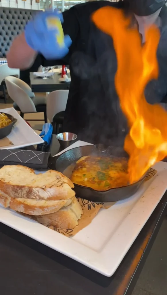 Traditional Greek saganaki cheese flambéed with dramatic orange flames at restaurant table with bread