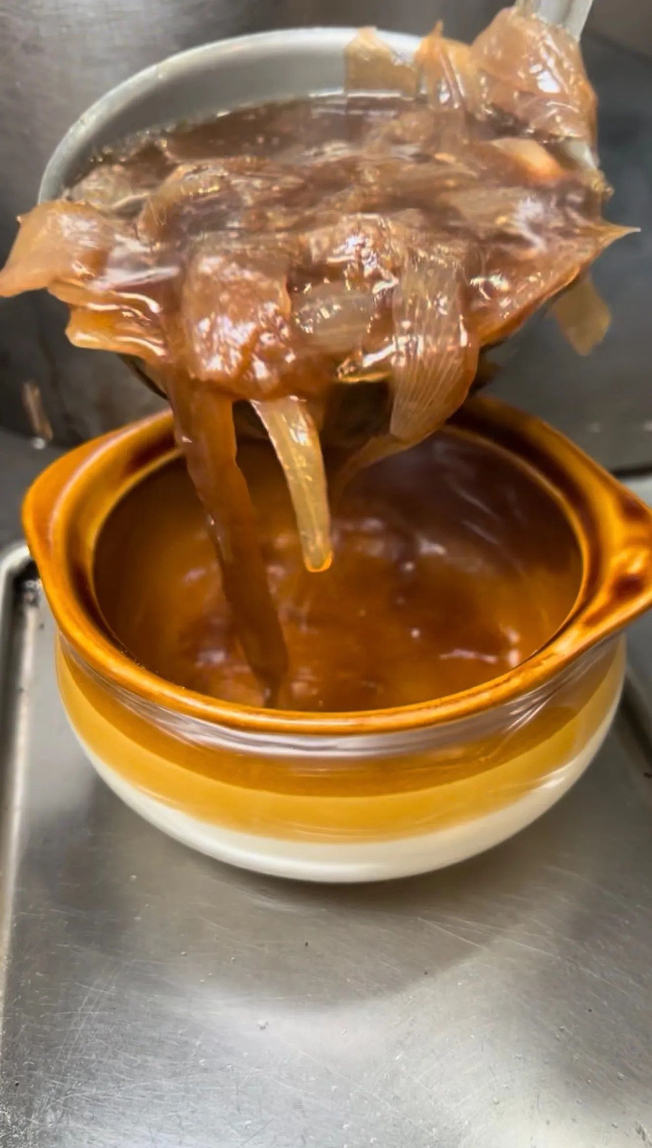 Caramelized onions being strained into a bowl for French onion soup