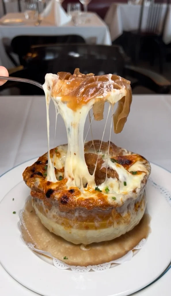 French onion soup with melted cheese stretching from spoon, served in white ceramic bowl on restaurant table