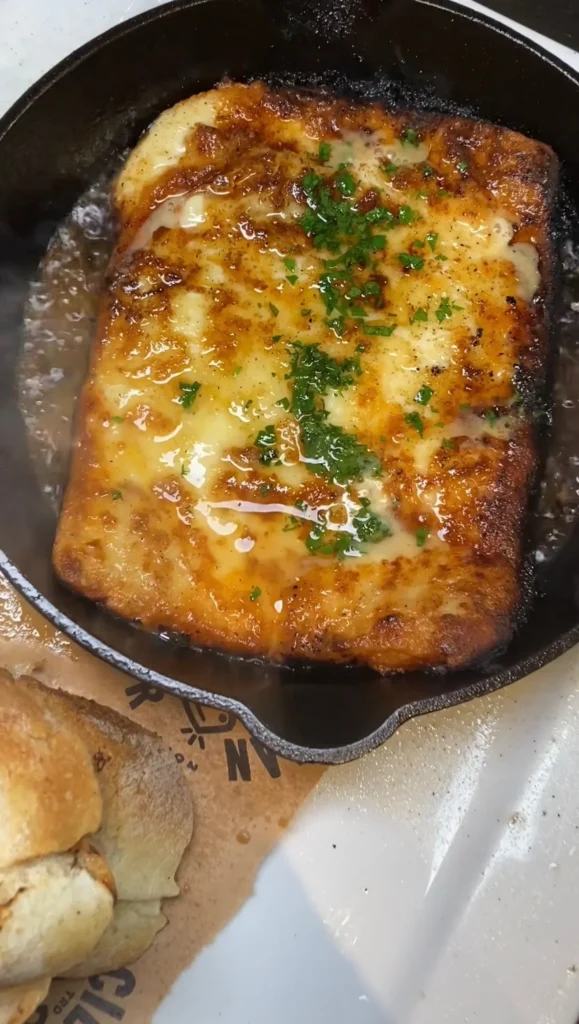 Golden bubbling Greek saganaki cheese garnished with fresh herbs in a black cast iron skillet