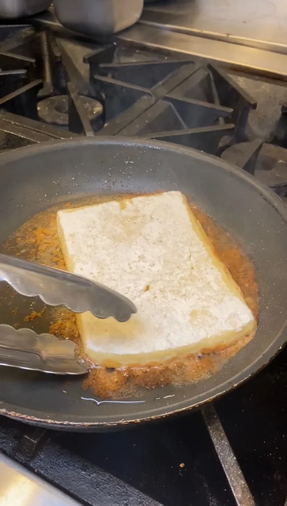 Traditional Greek saganaki cheese frying in a stainless steel pan on a commercial stovetop