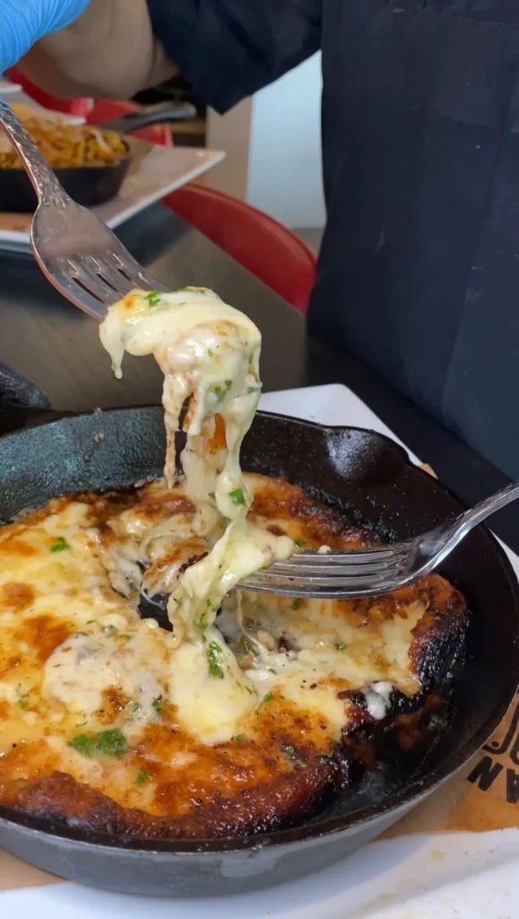 Traditional Greek saganaki with melted cheese stretching from fork in black cast iron skillet
