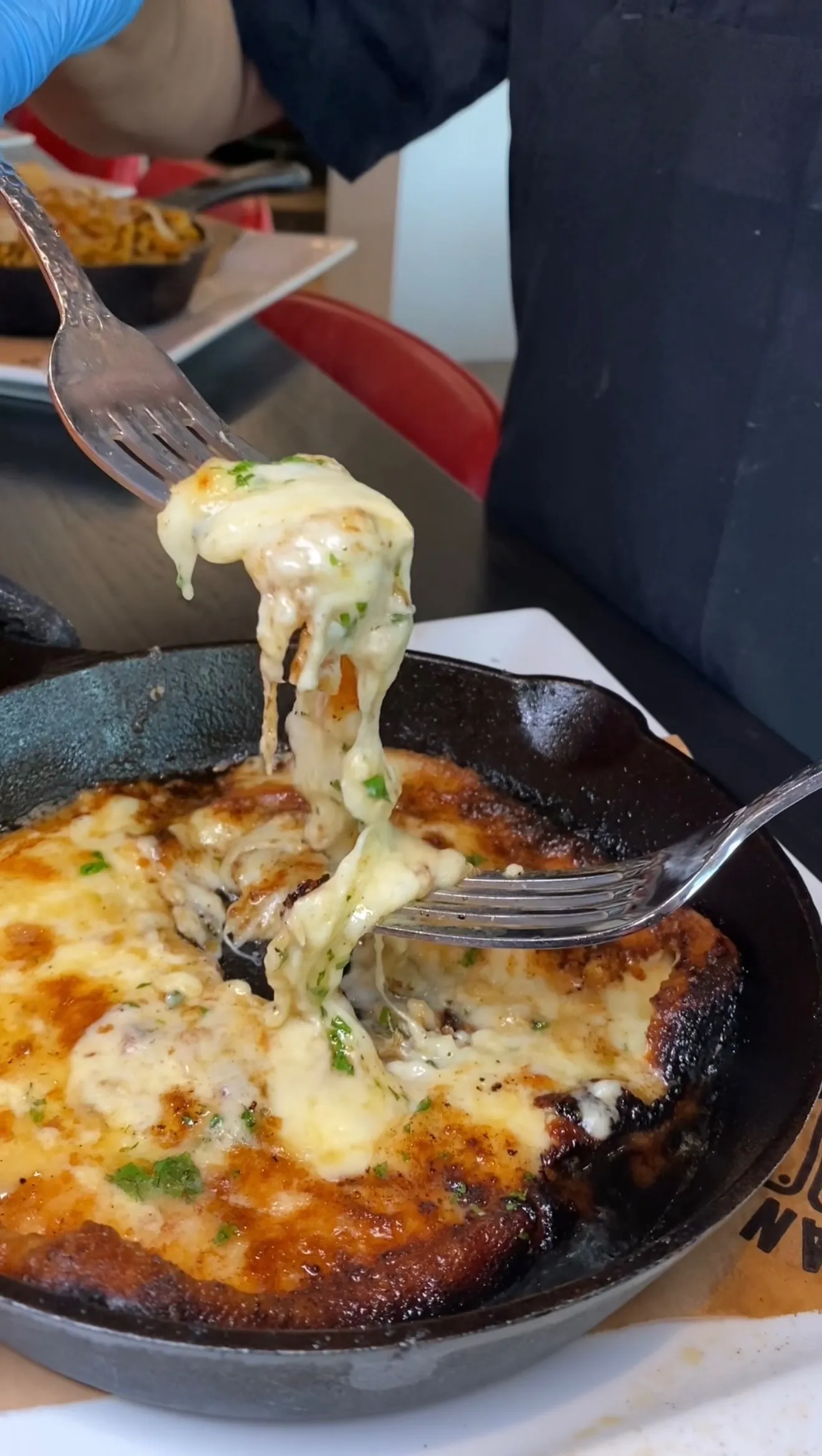 Traditional Greek saganaki with melted cheese stretching from fork in black cast iron skillet