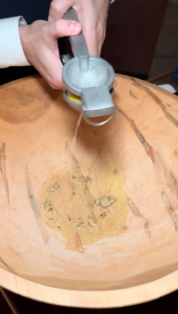 Hand using cheese grater to grate fresh Parmesan cheese into wooden salad bowl for Caesar salad preparation
