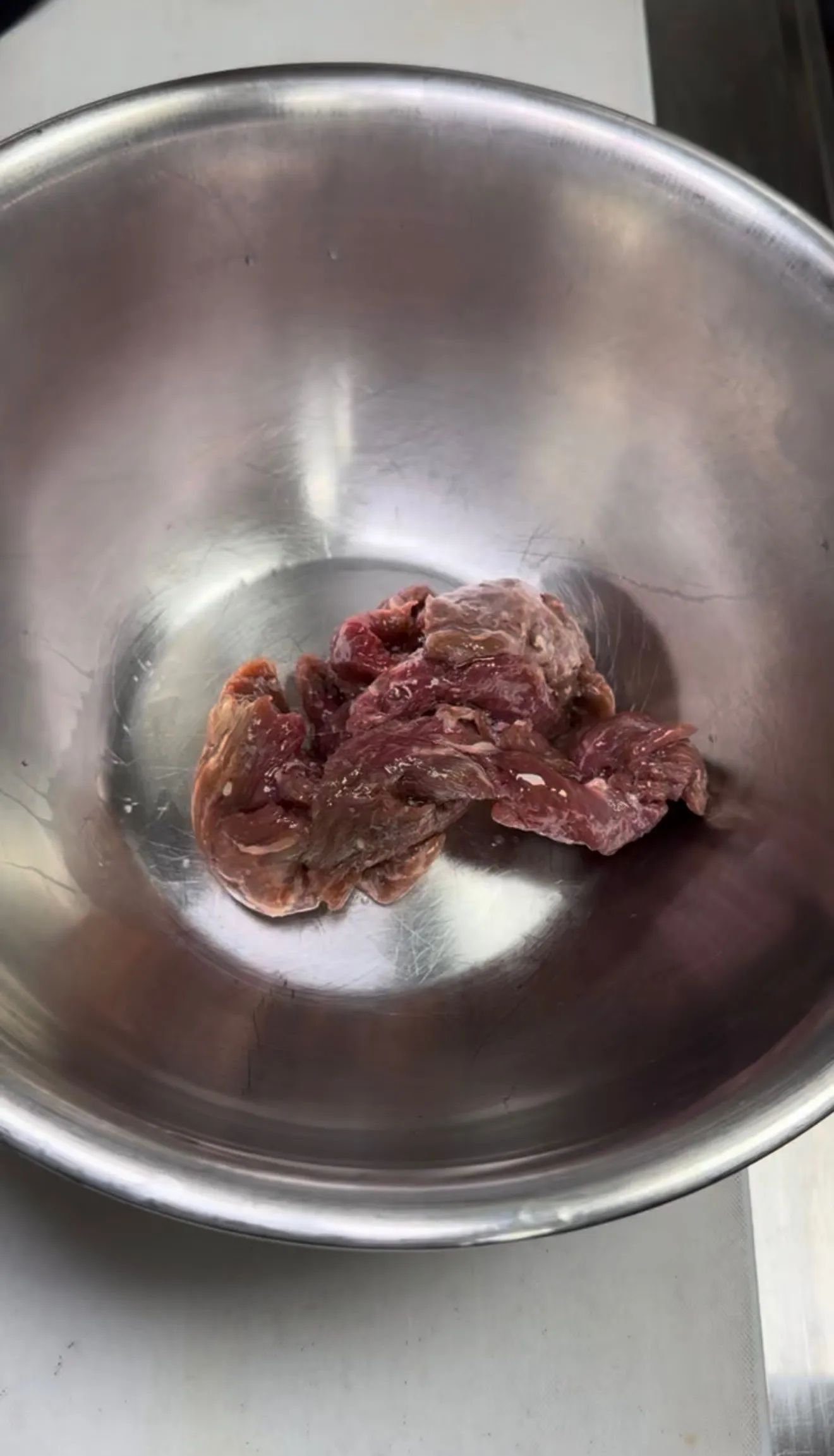Raw beef strips in a metal bowl seasoned for lomo saltado