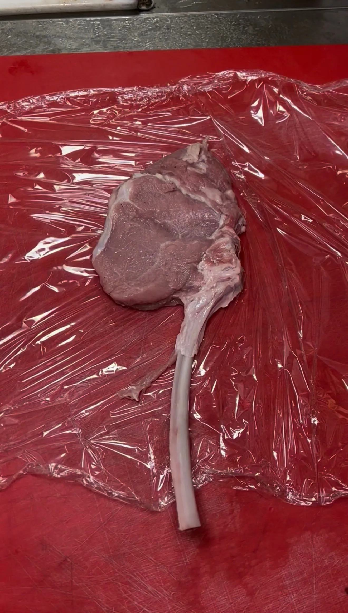Raw bone-in veal chop wrapped in plastic before pounding