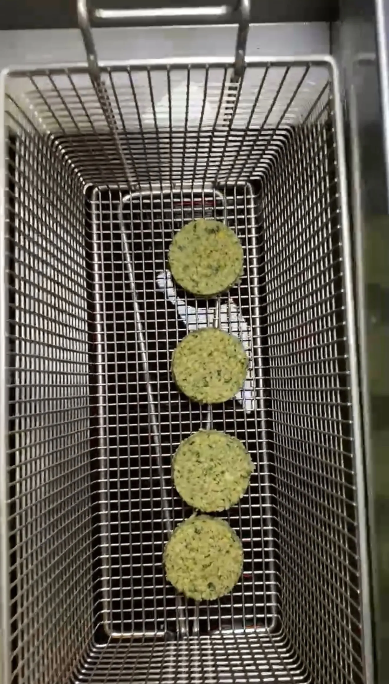 Raw falafel patties arranged in a fryer basket before cooking