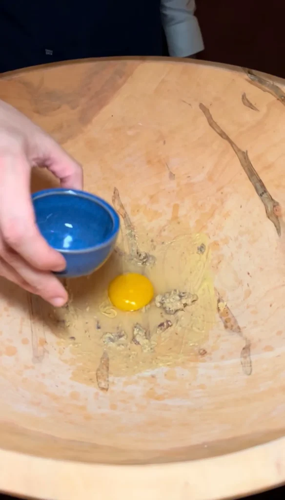 Fresh egg yolk separated in wooden bowl with blue egg separator for making Caesar salad dressing