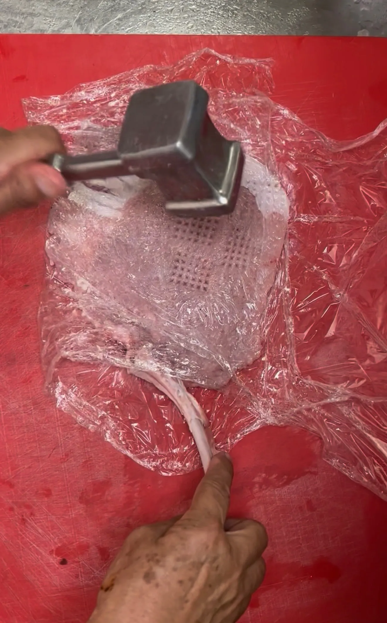Veal chop being tenderized with a meat mallet on a cutting board