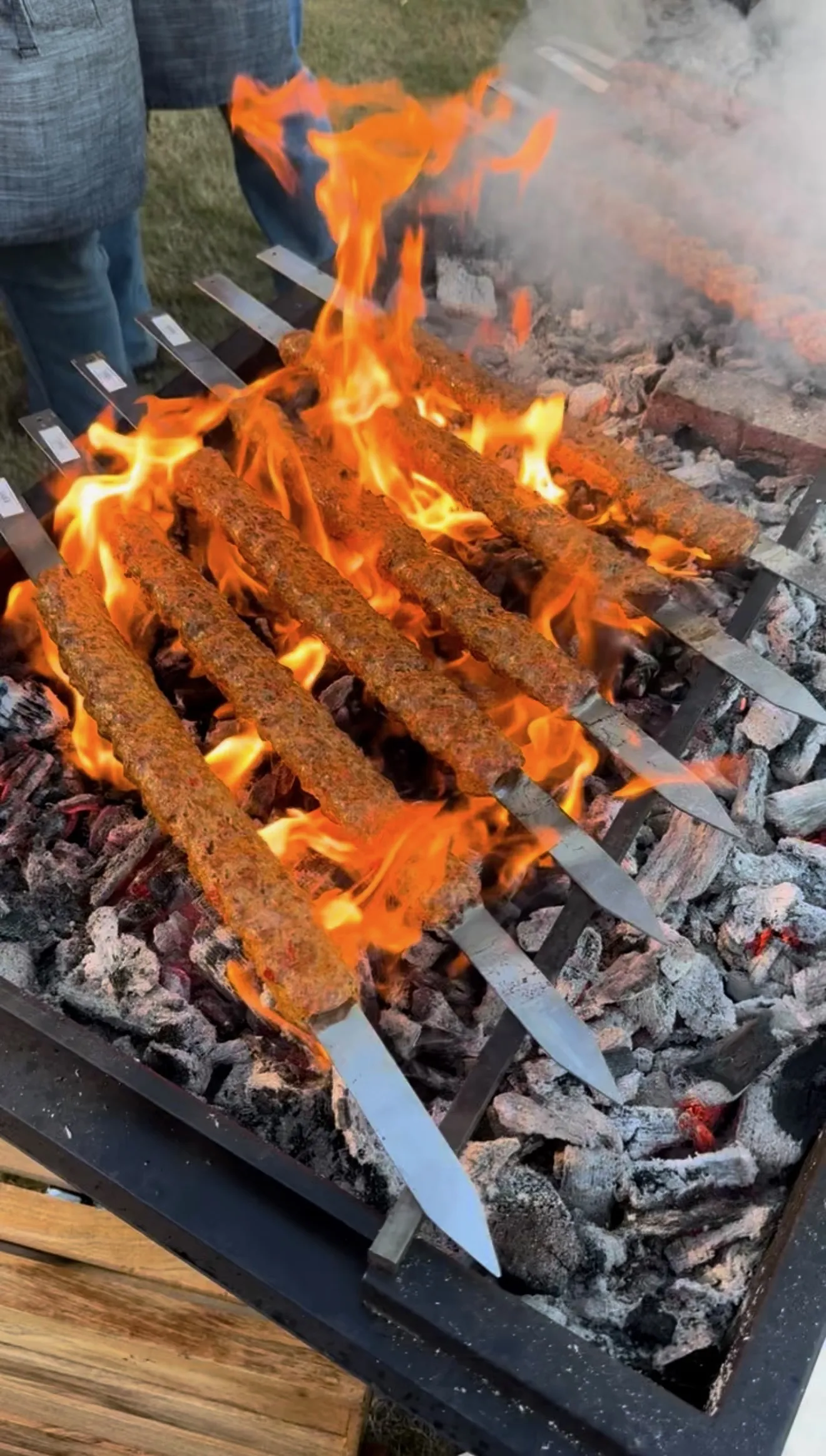 Adana kebab skewers grilling over open flames on a charcoal grill with bright orange fire