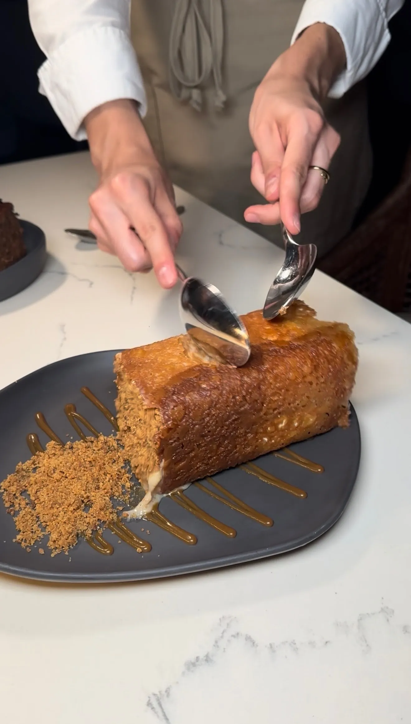 Chef plating Bananas in a Box dessert with caramel sauce and crumb garnish on dark plate