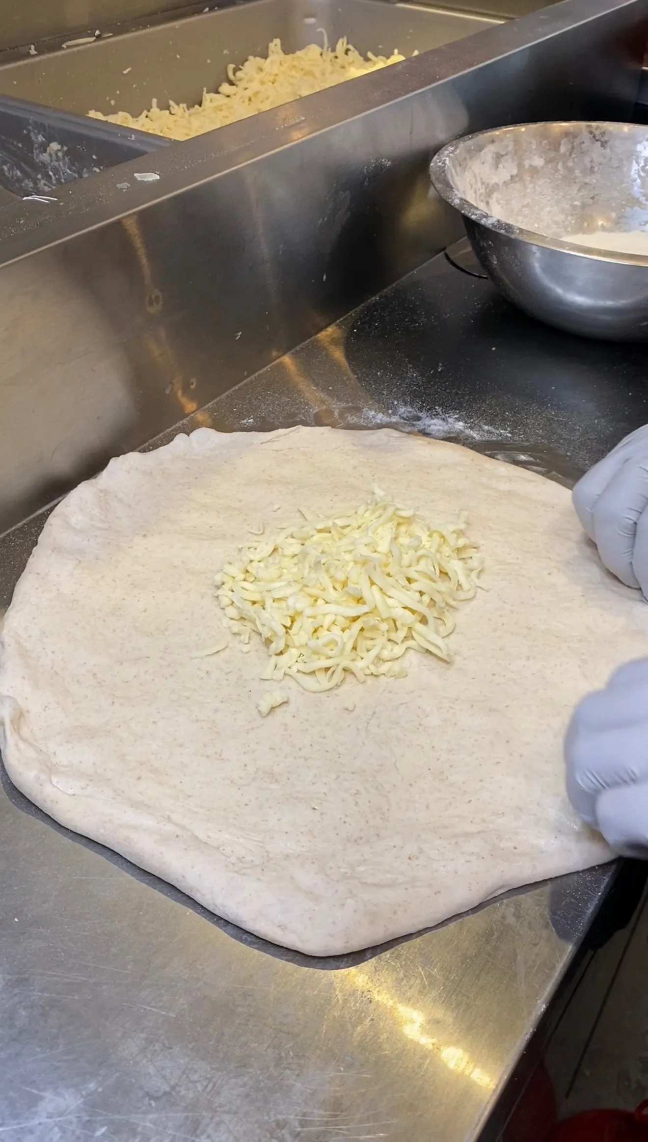 Pizza dough being filled with shredded cheese for calzone preparation