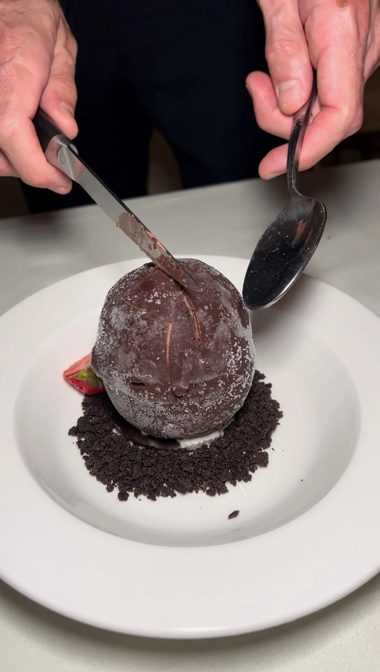 Chocolate shell tartufo being cracked open with spoons showing the interior