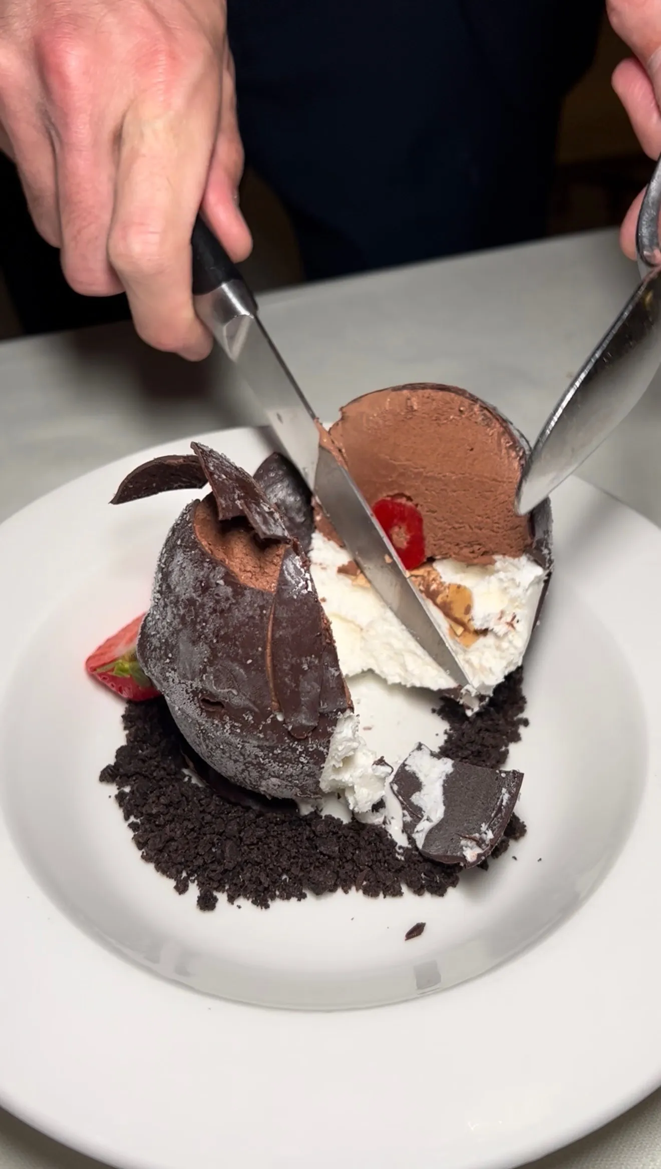 Chocolate shell tartufo being cut with knives showing the snap of the shell