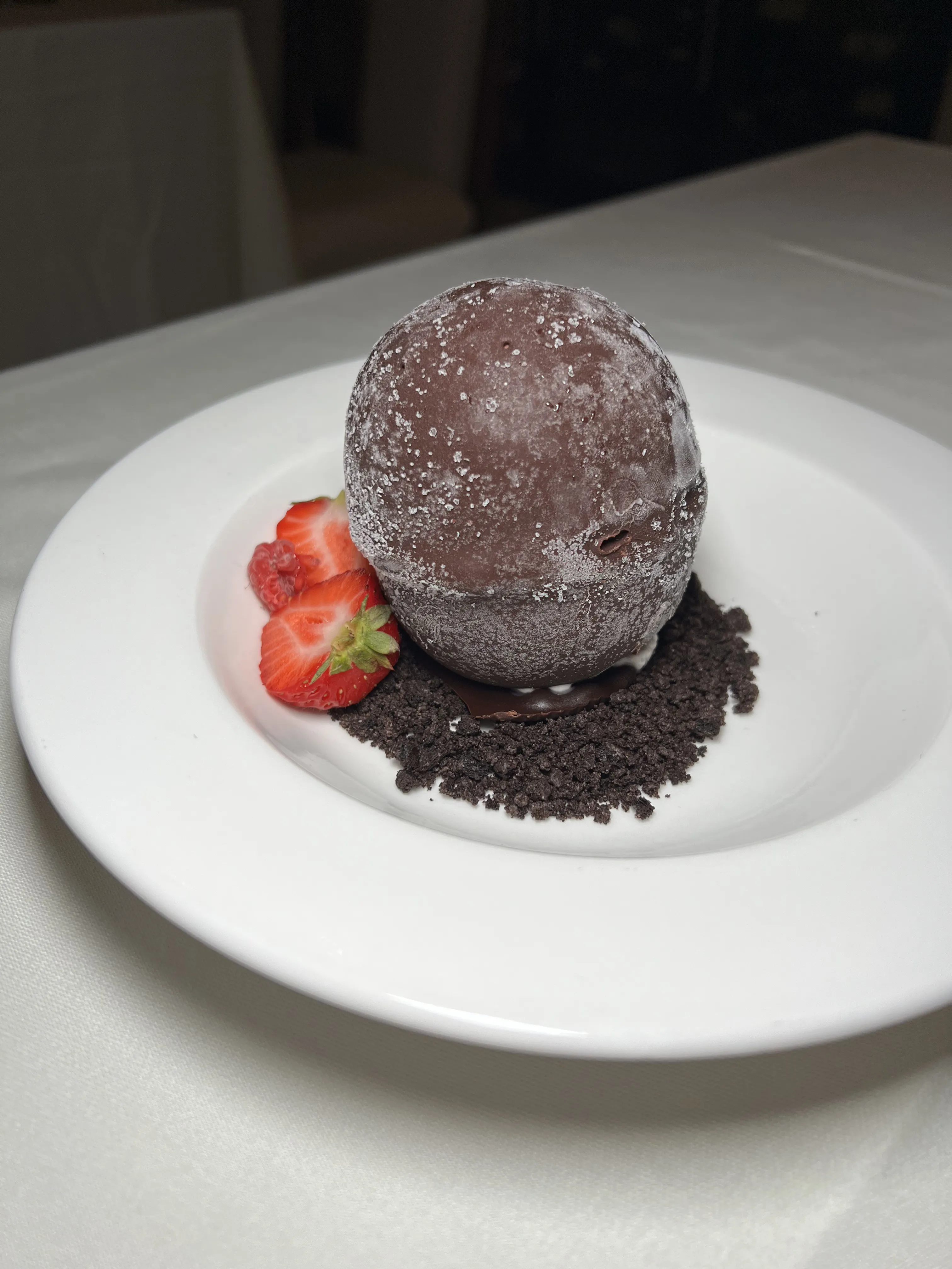 Chocolate shell tartufo plated with a strawberry garnish on a crumb base