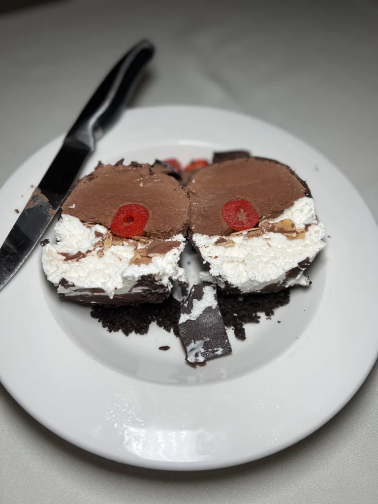 Sliced chocolate shell tartufo with white cream filling and red cherries on top, served on white plate with knife