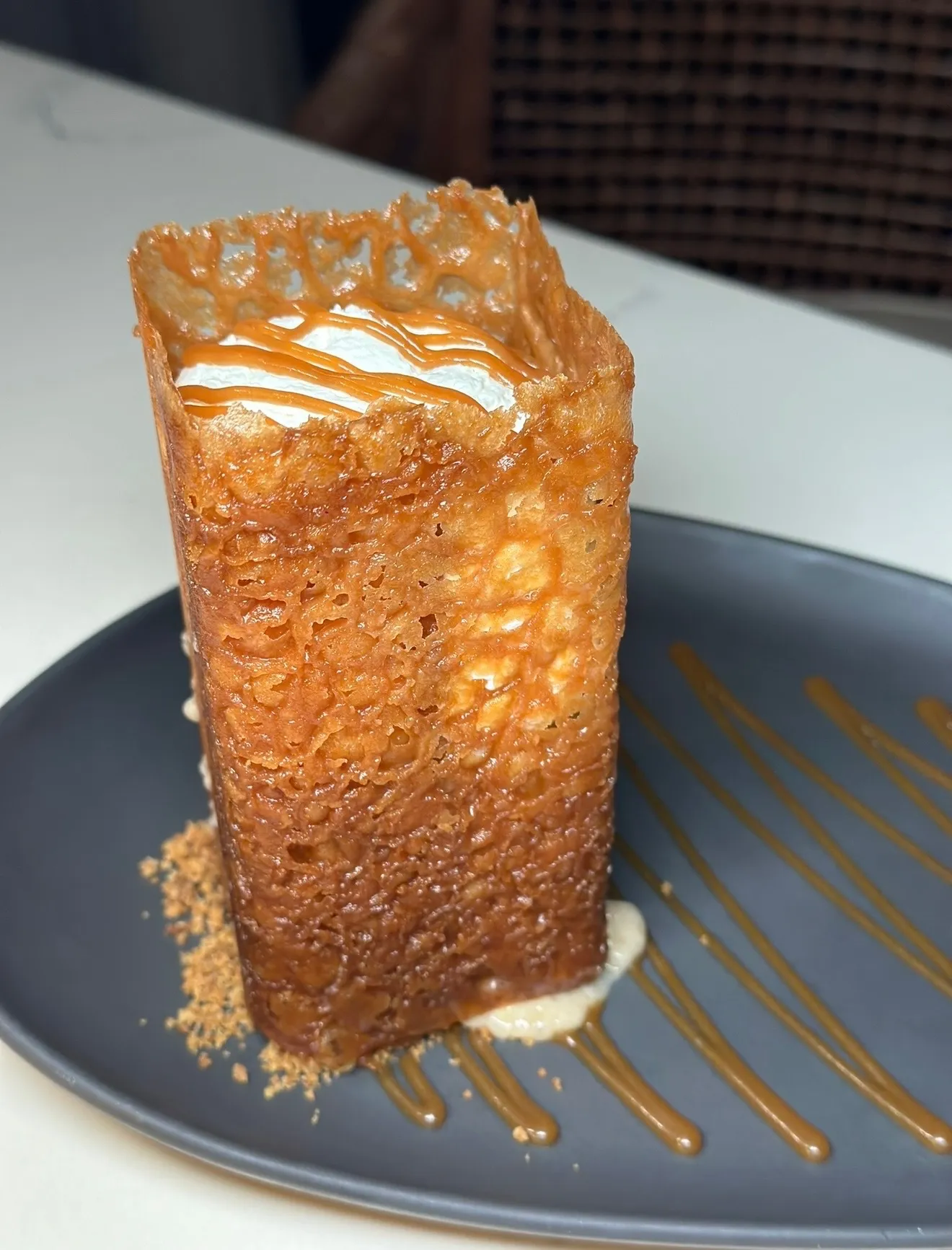 Golden crispy caramel cage tower filled with banana dessert on dark plate with caramel sauce drizzle