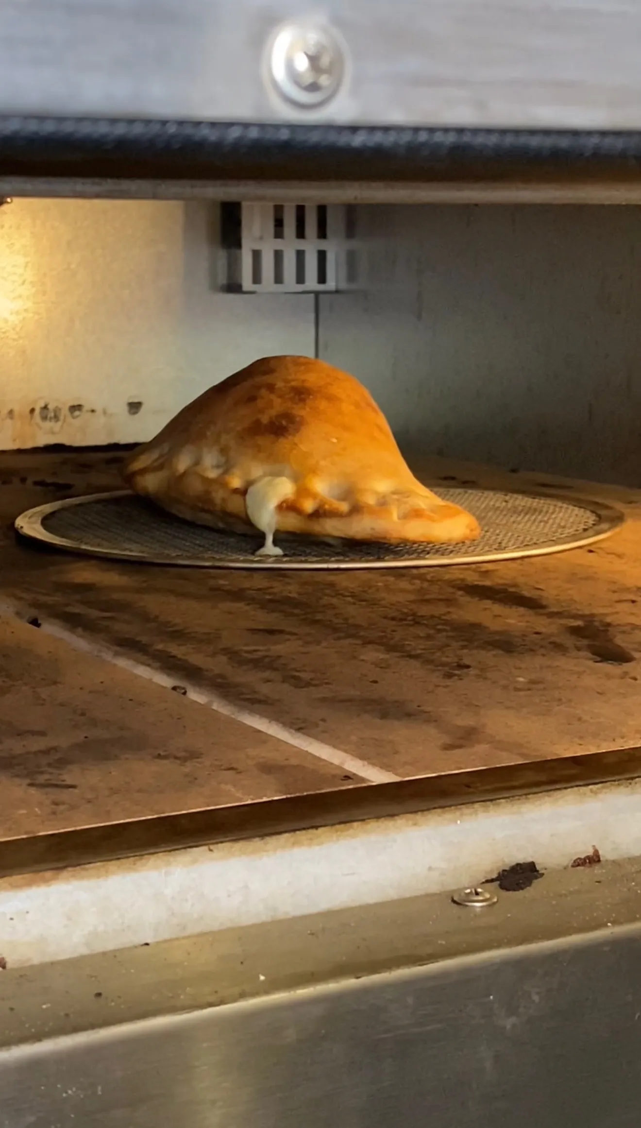 Golden-brown pepperoni three-cheese calzone with melted cheese oozing out on wire rack in oven