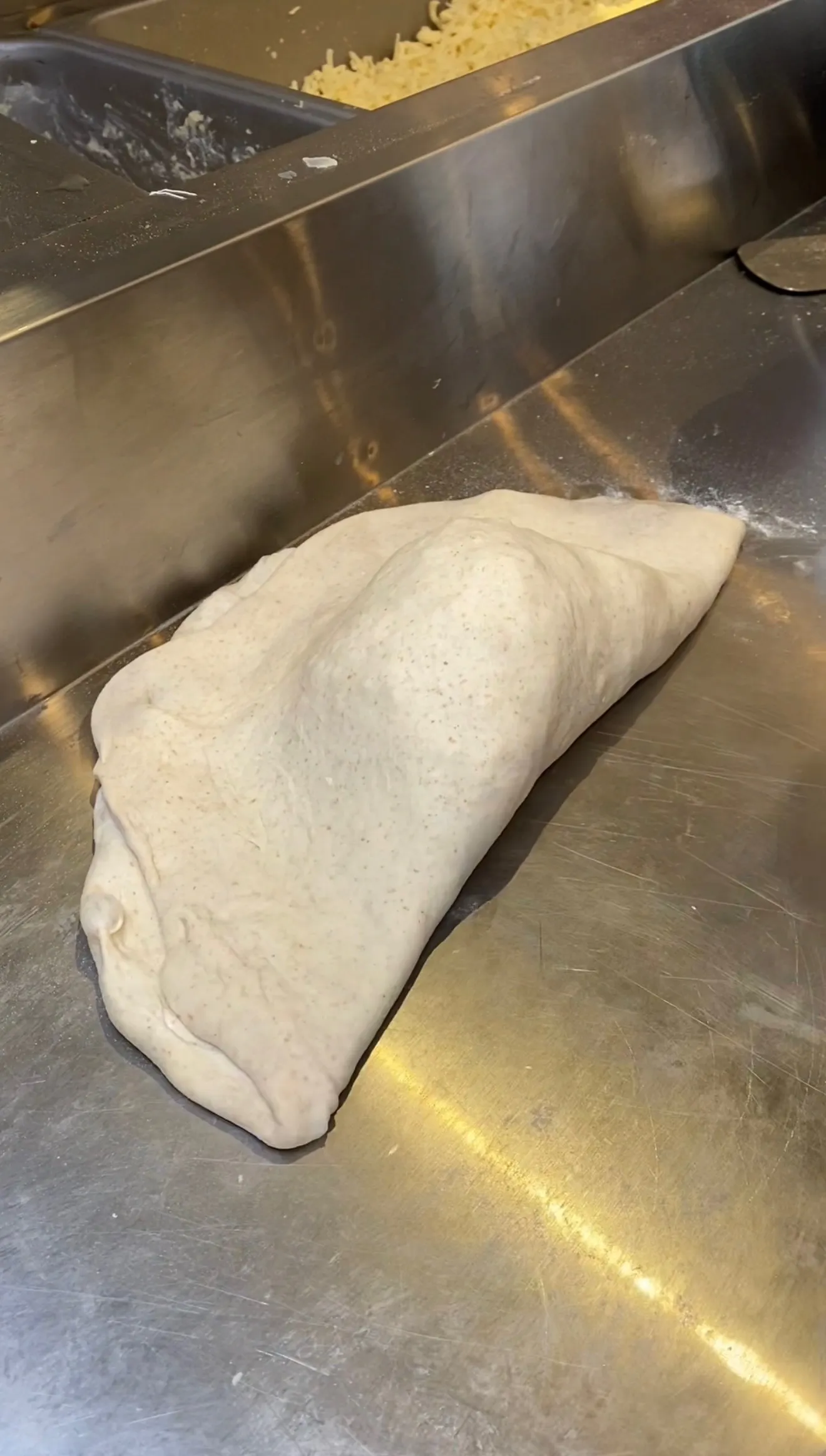 Folded pepperoni three-cheese calzone dough on stainless steel counter ready for baking