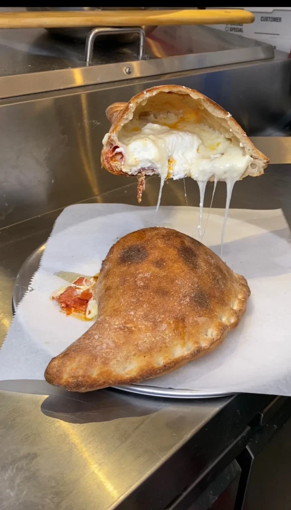 Homemade pepperoni three-cheese calzone cut in half showing melted cheese dripping onto parchment paper