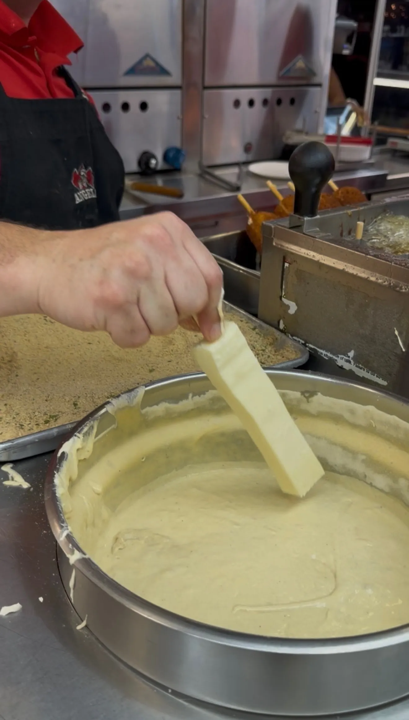 Mozzarella stick being dipped into thick batter for fair-style coating
