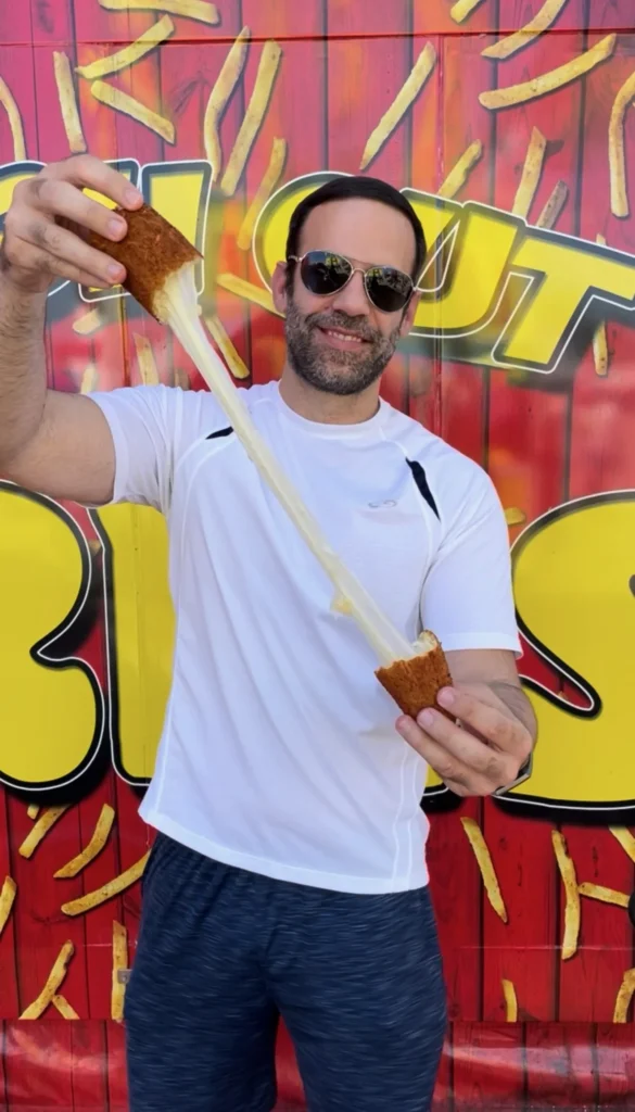 Person holding golden fried mozzarella stick showing stretchy melted cheese pull against colorful graffiti wall