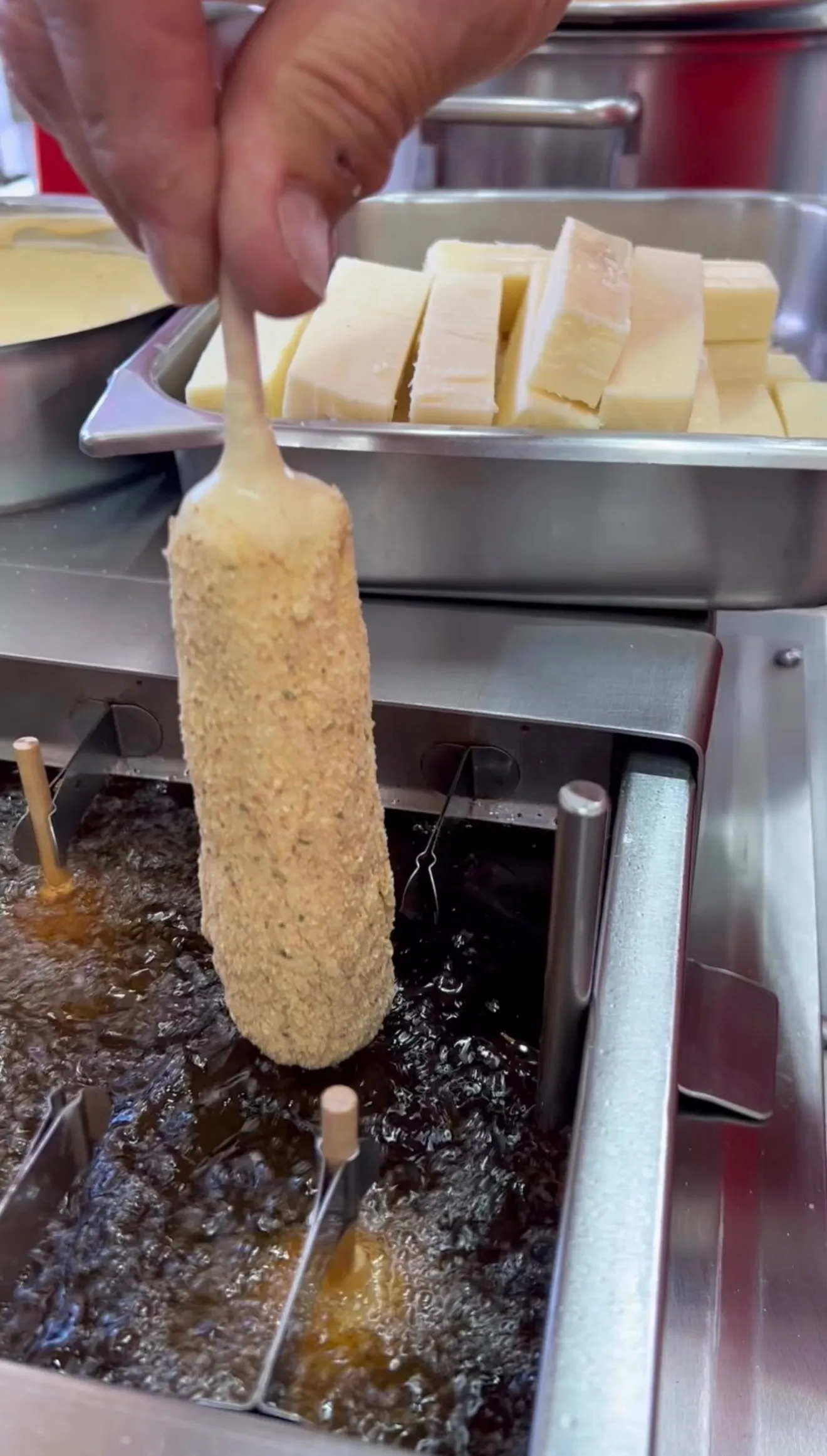 Thick battered mozzarella stick being deep fried in hot oil